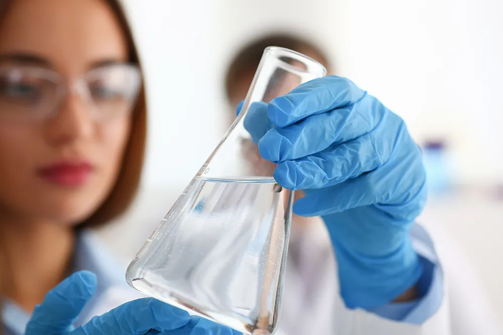 Hand of scientist holding flask with lab glassware in chemical laboratory background. Test your drinking water with the water testing kits from IVARIO.