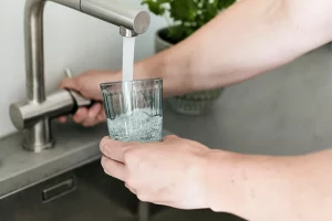 Person filling a glass with tap water at the tap. Test your drinking water with the water testing kits from IVARIO.